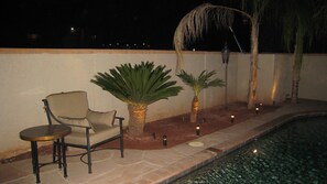 A poolside area with a chair, two palm plants, and a lamp post. - The Palm (Scottsdale)
