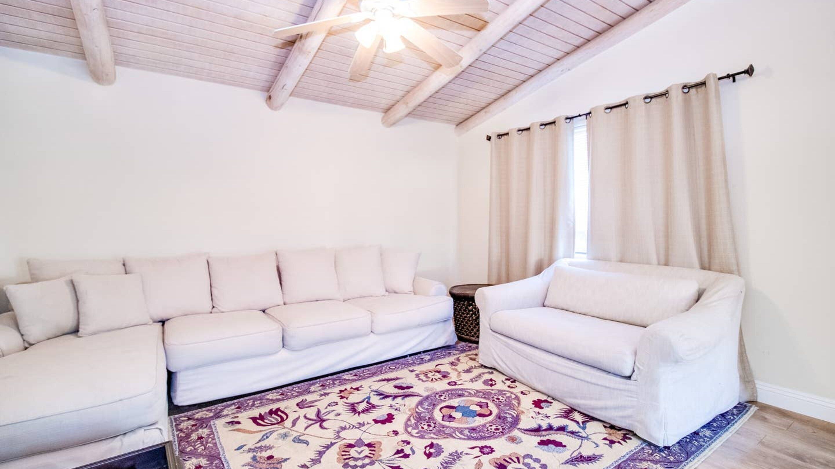 A living room with a white sofa, a smaller armchair, a patterned rug, and a ceiling fan.