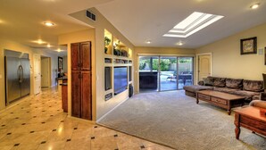 A spacious living area with a large couch, a coffee table, and a carpeted floor. There is a kitchen area with cabinets and a refrigerator. - Just Listed! Kierland Home w Htd Pool and Hot tub (Scottsdale)