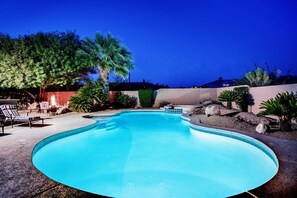 A swimming pool with a curved design, surrounded by a landscaped garden with various plants and a few lounge chairs. - Whisper Trail Resort (Scottsdale)