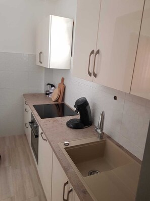 A compact kitchen with white cabinets, a black coffee maker, and a sink.