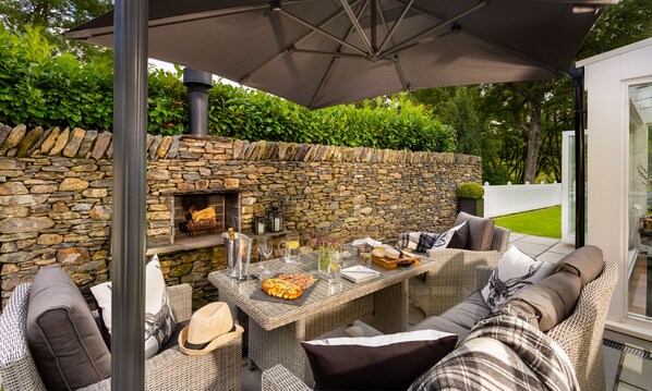 An outdoor patio with wicker furniture, a stone wall, and a grill.