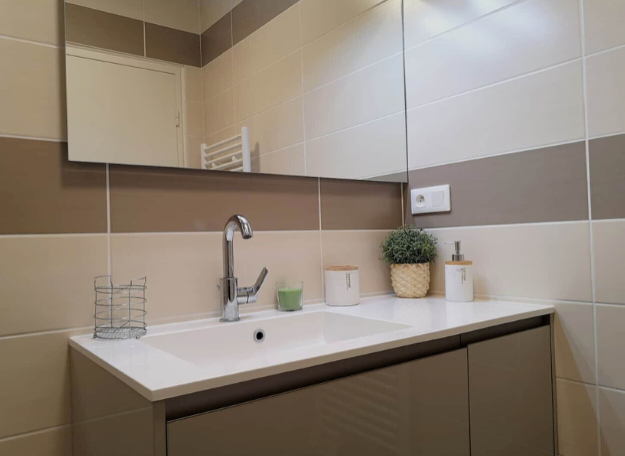 Une salle de bain avec un lavabo blanc, un miroir, un porte-serviettes et une plante en pot.