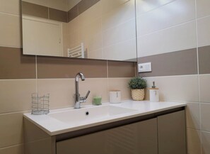 A bathroom with a white sink, a mirror, a towel rack, and a potted plant.