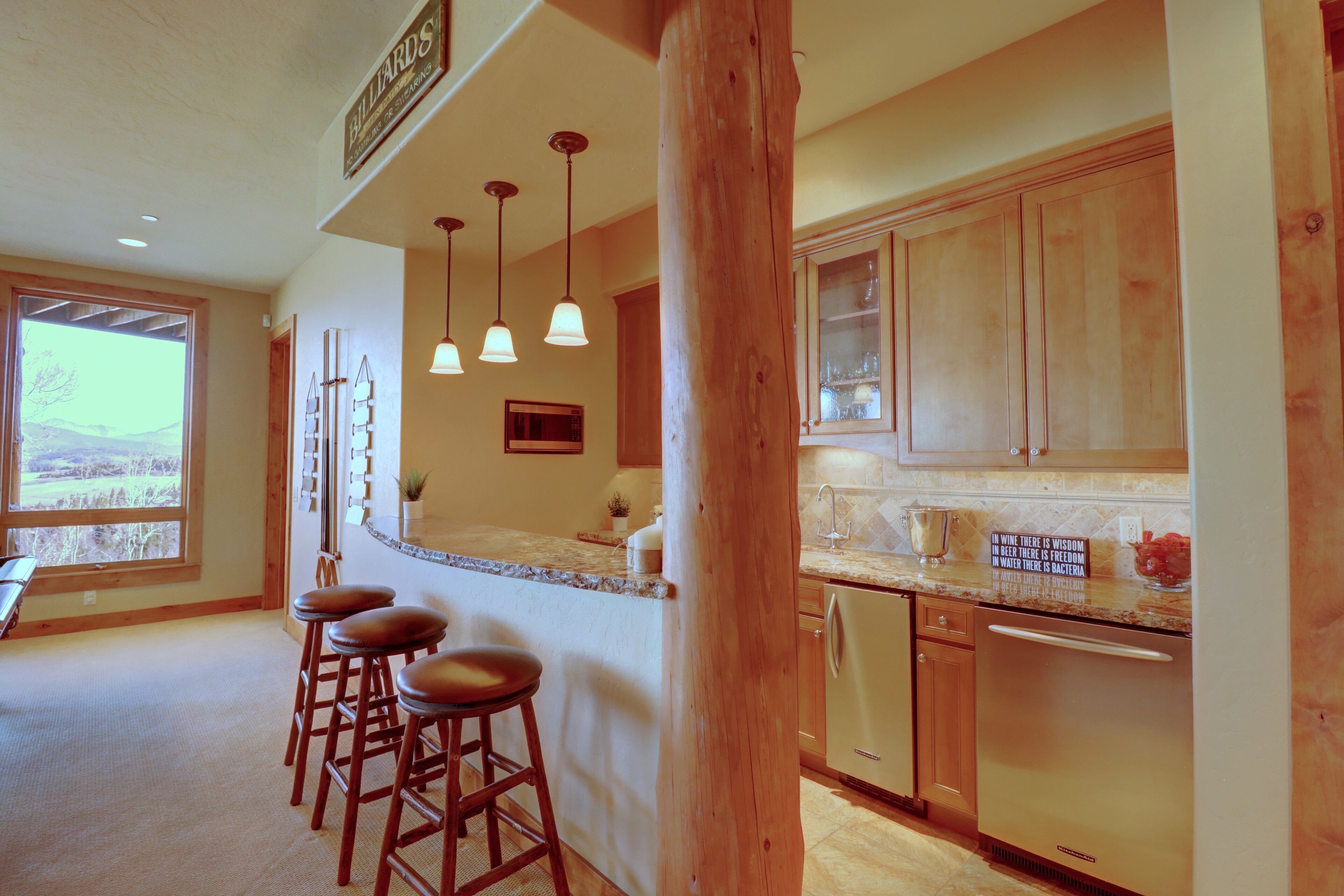 A kitchen with wooden cabinets, a bar area with stools, and a view of the outdoors.