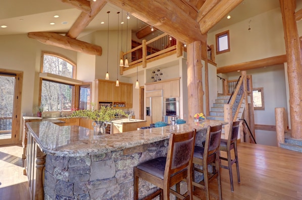 A spacious kitchen with a large island, wooden beams, and a stone countertop.