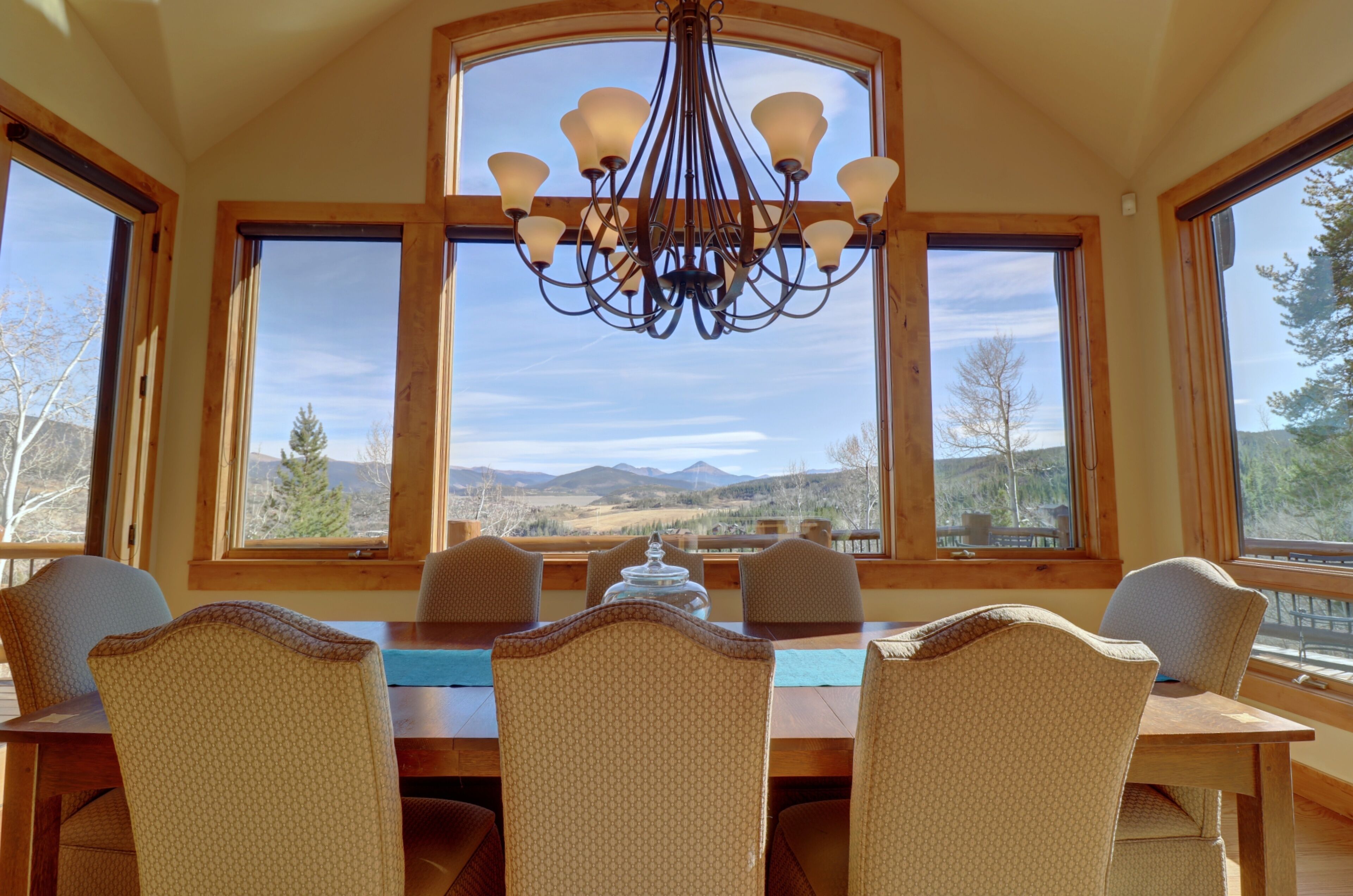 A dining area with a table and chairs, large windows with a view of mountains, and a chandelier.