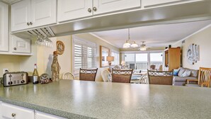 A kitchen with white cabinets, a granite countertop, and a dining area with wicker chairs and a table. - Ocean and Amelia Island View Condo with Oceanside Pool Access by RedAwning (Fernandina Beach)