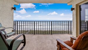 A balcony with a view of the ocean, a table, and two chairs. - Ocean and Amelia Island View Condo with Oceanside Pool Access by RedAwning (Fernandina Beach)