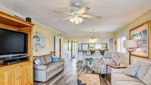 A spacious living room with a television, sofas, a coffee table, and a dining area with chairs and a table. - Ocean and Amelia Island View Condo with Oceanside Pool Access by RedAwning (Fernandina Beach)