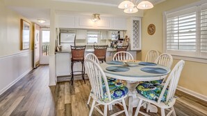 A dining area with a round table, white chairs, and a chandelier. - Ocean and Amelia Island View Condo with Oceanside Pool Access by RedAwning (Fernandina Beach)