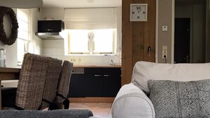 A living room with a white sofa, a patterned pillow, a wicker chair, and a kitchen in the background.