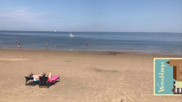 A beach with a few people and a sailboat in the distance.