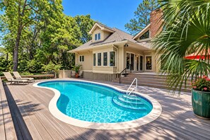 Una piscina con muelle de madera, rodeada de árboles y una casa con porche.
