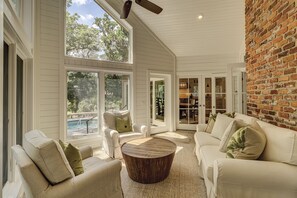 A spacious living area with a large window overlooking a pool, a brick wall, and a cozy seating arrangement.