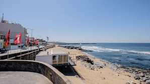A coastal beach scene with a modern building, a pier, and rocky shoreline.
