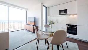 A modern kitchen with a glass dining table, white cabinets, and a view of the beach.