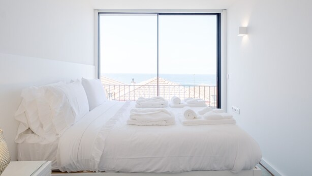 A hotel room with a large window, a neatly made bed, and a view of the beach.