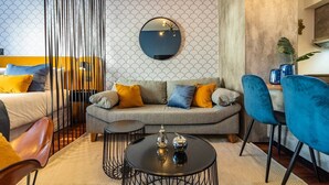 Ein modernes Wohnzimmer mit einem grauen Sofa, blauen und gelben Kissen, einem runden Couchtisch und einem großen Spiegel an der Wand.