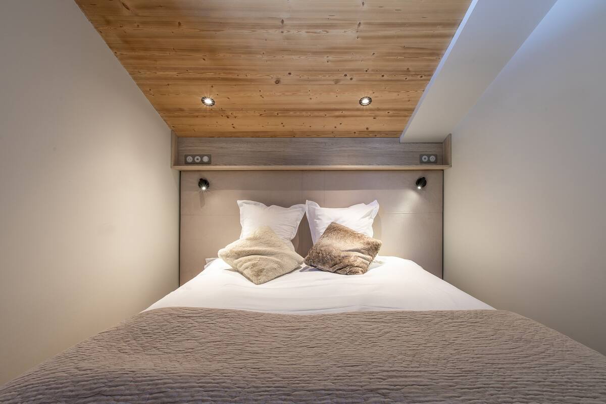 Un dormitorio con techo de madera, cama con manta texturizada y dos almohadas.