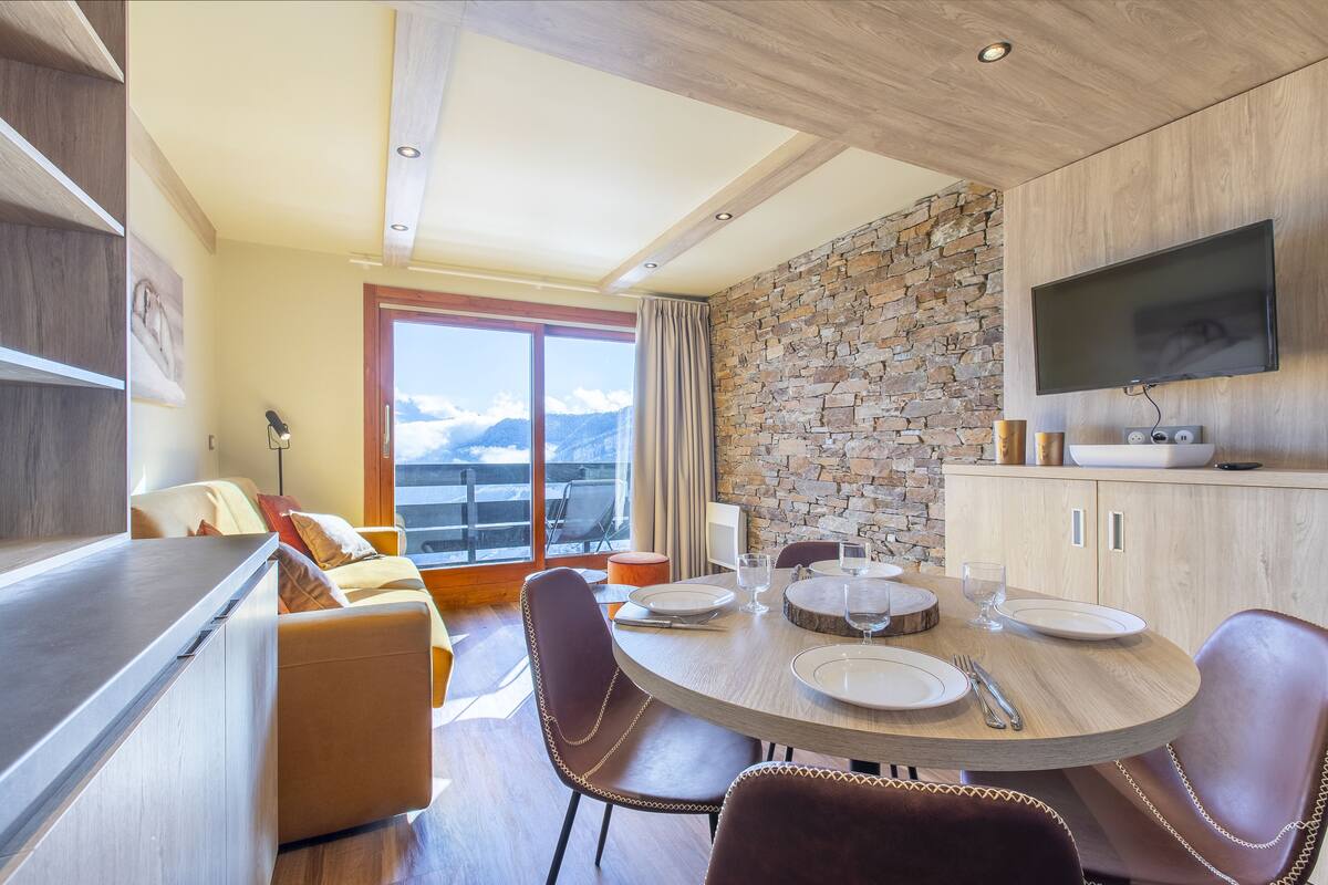 Un comedor moderno con pared de piedra, techo de madera y un ventanal con vistas a la montaña.