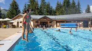 A swimming pool area with a building in the background, surrounded by trees. - Vacancéole - Résidence La Duit (Esserts-Blay)