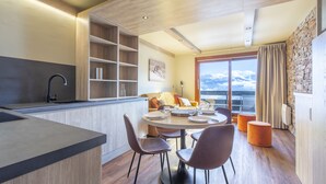 A modern kitchen with a central island, dining area with chairs, and a large window with a view. - Vacancéole - Résidence La Duit (Esserts-Blay)