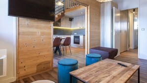 A modern interior with wooden walls, a dining area with blue stools, a wooden table, and a staircase leading to an upper level. - Vacancéole - Résidence La Duit (Esserts-Blay)