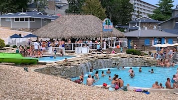 Un espace piscine agrémenté d’une structure à toit de chaume, d’un panneau indiquant « Tiki Hut », et d’une cascade artificielle.