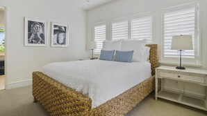 A bedroom with a large bed, white walls, and a window with blinds. There are two framed pictures on the wall and a bedside table with a lamp. - New Downtown Petoskey Custom Home.  (Petoskey)