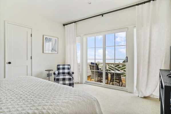 A hotel room with a large bed, a chair, a small table, and a balcony with a view of the sky and a distant landscape. - New Downtown Petoskey Custom Home. (Petoskey)