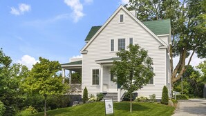 A two-story white house with a green roof, a front porch, and a signboard. - New Downtown Petoskey Custom Home.  (Petoskey)