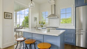 A modern kitchen with a large island, bar stools, a stainless steel refrigerator, and a view of the outdoors. - New Downtown Petoskey Custom Home.  (Petoskey)