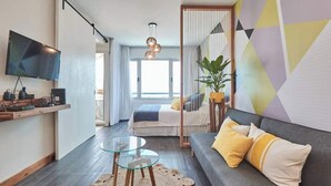 Habitación de hotel moderna con sofá, una mesita de cristal, televisor y un ventanal con vistas al mar.