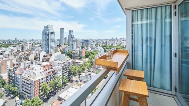 Un balcón con vista a un paisaje urbano, incluyendo edificios altos y cielo despejado.