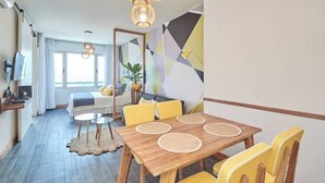 Una habitación de hotel moderna con una mesa de comedor de madera, sillas amarillas, un espejo grande y una pared con un diseño geométrico.