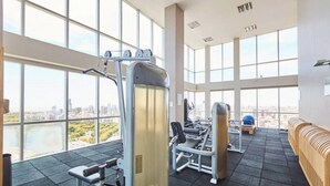 Un gimnasio con amplios ventanales, equipamiento de ejercicio y vistas a un paisaje urbano.