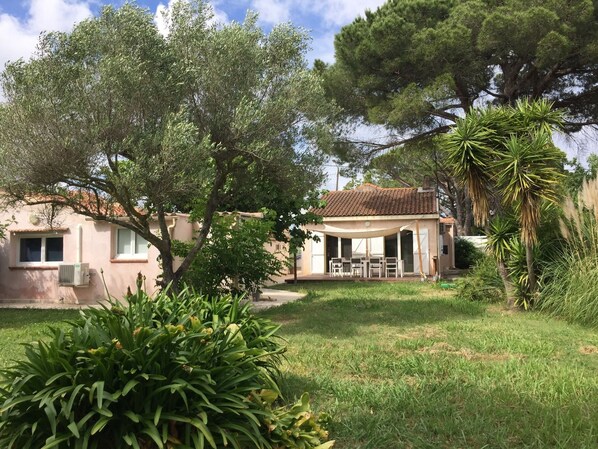 A house with a patio, surrounded by trees and greenery. - Air-conditioned beach house: 7-minute walk, fenced-in yard, charging station for electric cars (Hyères)