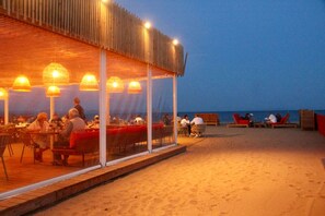 An outdoor dining area with tables and chairs, a covered seating area with red cushions, and a view of the sea. - Air-conditioned beach house: 7-minute walk, fenced-in yard, charging station for electric cars (Hyères)