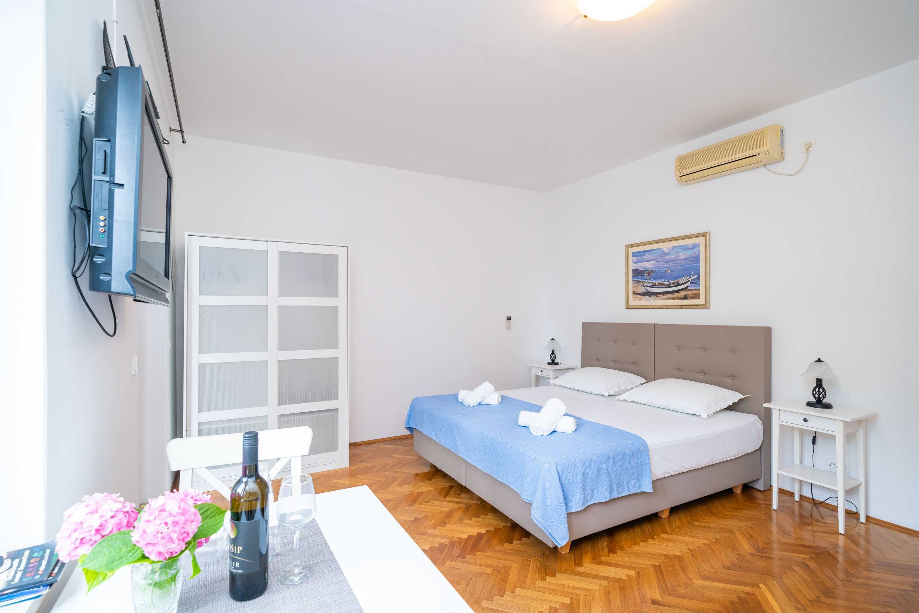 Une chambre à coucher avec un lit, un téléviseur fixé au mur, une fenêtre et un tableau accroché au mur.