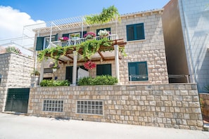 A two-story building with a stone facade, a balcony with hanging plants, and a window with shutters. - Villa Ivka (Dubrovnik)
