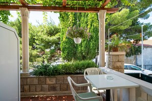 Un espacio al aire libre cubierto con una mesa y sillas, rodeado de vegetación y un muro de piedra.