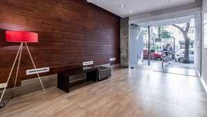 Un vestíbulo moderno con pared de madera, una lámpara de pie roja, un banco y una puerta de cristal que da al exterior.