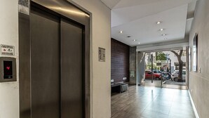 Un ascensor moderno con pantalla digital, un área de recepción con un banco y vistas a coches estacionados afuera.