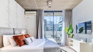 Una habitación de hotel moderna con una cama grande, un televisor de pantalla plana, un balcón con vistas a la ciudad y un equipo de aire acondicionado.