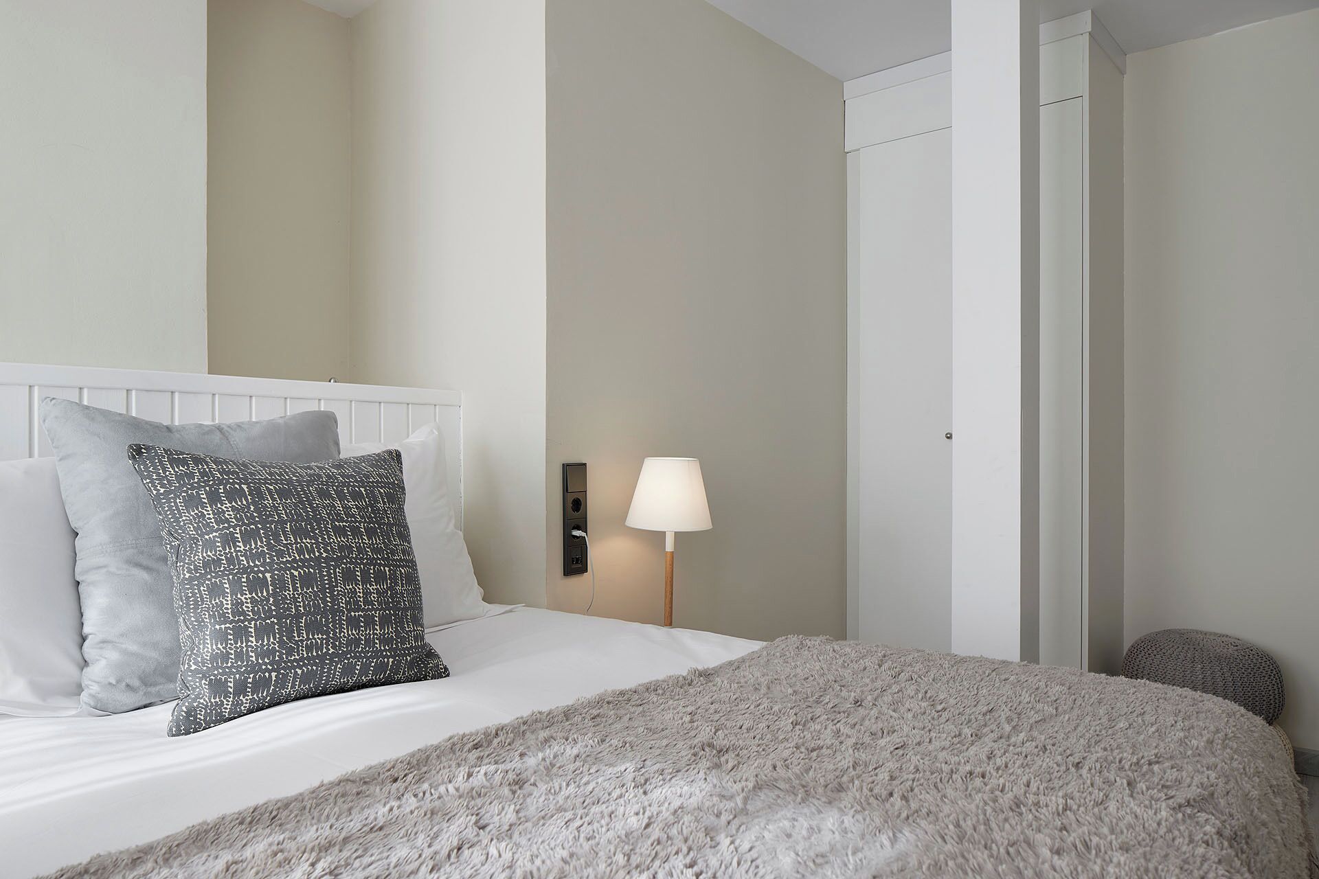 Una cama bien hecha con almohadones estampados, un edredón gris esponjoso y una lámpara de noche.