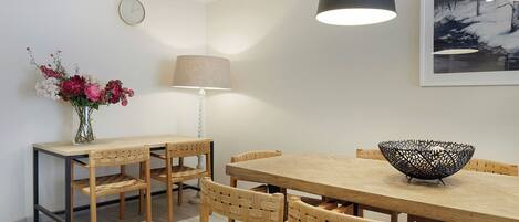 Un comedor con una mesa y sillas de madera, un florero con flores, una lámpara y un cuadro en la pared.
