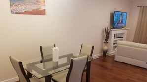 A dining area with a glass table and four chairs, a television on a stand, and a sofa in a living room. - Stylish Heritage 5 BR House  Ideal For Long Stays - With Jacuzzi (Fort McMurray)