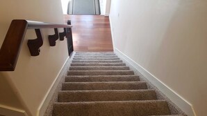 A carpeted staircase with a wooden handrail leading to a room with a wooden floor. - Stylish Heritage 5 BR House  Ideal For Long Stays - With Jacuzzi (Fort McMurray)