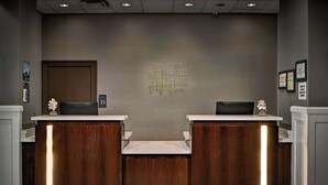 Una zona de recepción con dos mostradores de madera, una pared neutra con una obra de arte geométrica y diplomas enmarcados.